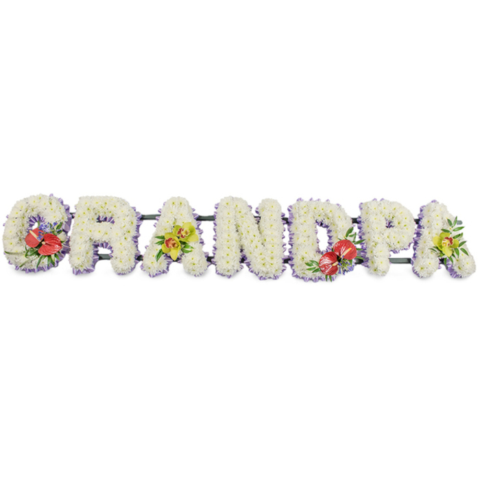 Set against a plain white backdrop, a dignified floral tribute stretches in a single horizontal line, spelling GRANDPA in robust block capitals made entirely from fresh white blooms. Each letter is built on a green frame yet appears soft and cloud-like, thanks to the tight carpeting of small chrysanthemum heads that cover every surface. The petals are crisp and clean, a pure white that suggests innocence, reverence, and peace, particularly powerful when seen at a funeral or memorial gathering. Along the base of each letter, a narrow border of pale lilac or lavender ribbon creates a gentle underline, helping the forms stand out and adding a whisper of colour without overwhelming the calm palette. Fine green metal or wooden bars join the letters at the back, providing the hidden strength needed for display at a church, crematorium, or graveside in Chigwell and neighbouring areas such as Buckhurst Hill. Carefully placed clusters of accent flowers introduce richness and depth. On the far left, the 'G' carries a bold grouping of red anthuriums, their waxy, heart-shaped surfaces shining softly, surrounded by deep green foliage and touches of smaller purple flowers. Near the centre, the 'D' mirrors this treatment with another vivid cluster of anthuriums, balancing the word visually. The first 'A' and final 'A' are crowned with yellow-green orchids, their exotic petals arching gracefully over the white cushion of chrysanthemums, evoking enduring love and cherished memories. This GRANDPA tribute feels both classic and contemporary, a personalised memorial piece that would sit beautifully beside a coffin or at the front of a service, expressing respect, warmth, and appreciation for a grandfather's life.