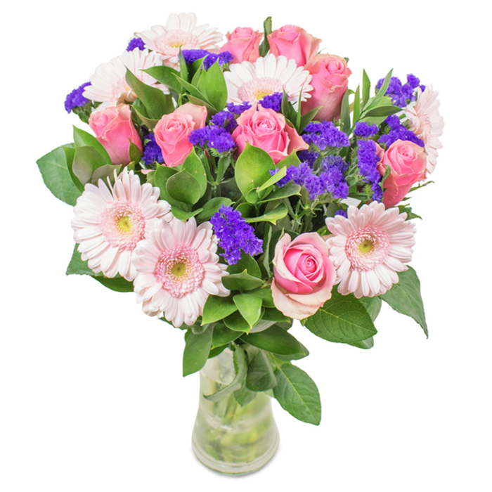 In this striking floral arrangement crafted in Chigwell, a sense of classical elegance meets modern warmth. Approximately 7-9 perfectly spiraled pink roses-some shyly furled, others just opening to reveal their iconic whorls-anchor the centre of the bouquet. They're accompanied by 5-7 pale pink Gerbera daisies, their bold, round faces radiating gentle joy with almost white, sunlit centres. Between the larger blooms spill clouds of vivid purple filler, likely statice, infusing lively texture and a daring splash of colour, reminiscent of the wild blooms bordering Chigwell Golf Club. The base, a lush weave of deep green foliage, supports the entire composition, offering rich depth and a hint of woodland scent that conjures nearby recreational walks. Arranged in a pristine clear glass vase-stems and crystal-clear water visible-this bouquet appears as fresh as if delivered directly from the market stalls on Chigwell High Road. Whether for a birthday, anniversary, Mother's Day, or simply as a gesture of celebration, the visual harmony and fragrant abundance evoke pure affection and local pride. It's more than a bouquet; it's a handcrafted expression of joy and care that brightens any room or heart across Chigwell.